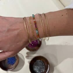 Poignet orné de plusieurs bracelets dorés et d’un bijou en perles colorées fabriqués à l’atelier.